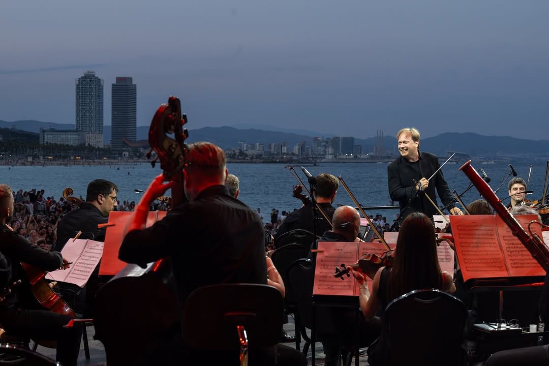Fotografía nocturna del festival Clàssica a la Platja, mostrando a la orquesta en plena interpretación y el público siguiendo las actuaciones desde la arena.
